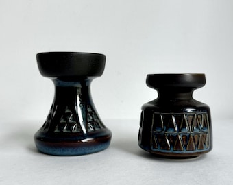 May include: Two ceramic candle holders. The larger one is dark blue with a geometric pattern and a black top. The smaller one is dark brown with a geometric pattern and a blue accent. Both have a glossy finish.