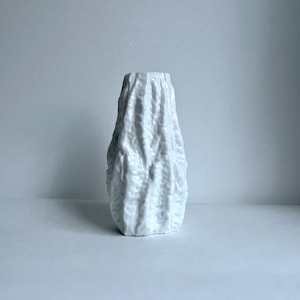 May include: White ceramic vase with a textured, organic design. The vase has a rounded, bulbous shape and a narrow opening.