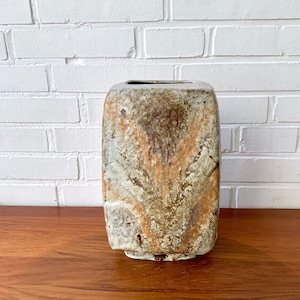 May include: A square ceramic vase with a textured, mottled glaze in shades of brown, white, and orange. The vase has a slightly irregular shape and a wide opening.