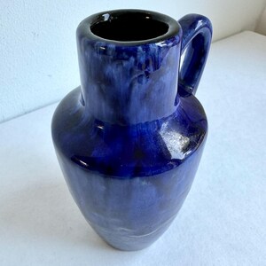 May include: A blue ceramic vase with a handle. The vase has a mottled glaze with a dark blue base and lighter blue streaks.
