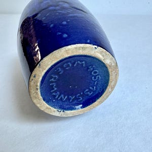 May include: A dark blue ceramic vase with a white rim and the text "MANYS'S" in a circle on the bottom.