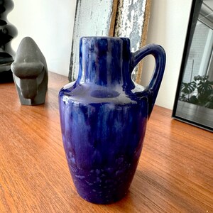 May include: A blue ceramic vase with a textured glaze. The vase has a wide base and a narrow neck with a handle.