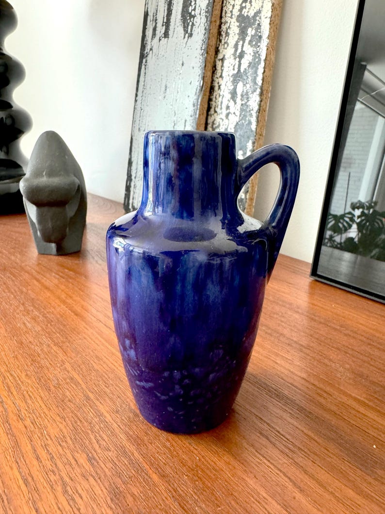 May include: A blue ceramic vase with a textured glaze. The vase has a wide base and a narrow neck with a handle.