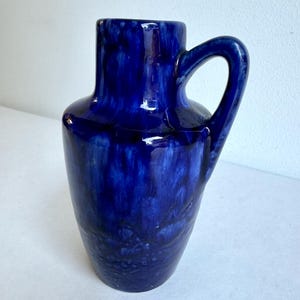 May include: A cobalt blue ceramic vase with a single handle. The vase has a mottled glaze with a slightly textured surface.