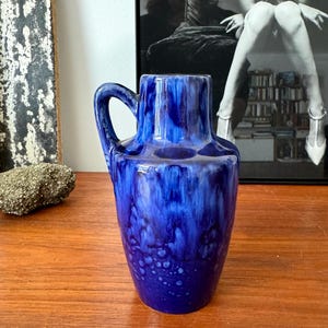 May include: A blue ceramic vase with a white glaze and a handle. The vase has a mottled blue and white design.