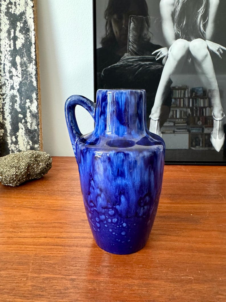 May include: A blue ceramic vase with a white glaze and a handle. The vase has a mottled blue and white design.