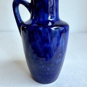 May include: A blue ceramic vase with a handle. The vase has a mottled blue glaze with white and black accents.
