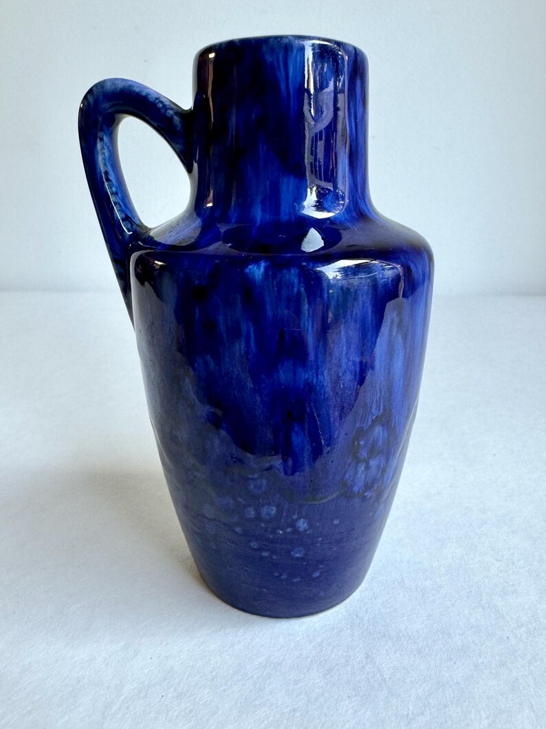 May include: A blue ceramic vase with a handle. The vase has a mottled blue glaze with white and black accents.