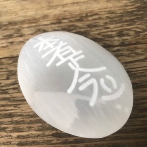 Pode incluir: Ovo de cristal de selenite branco com o s&iacute;mbolo chin&ecirc;s do "amor" gravado nele.