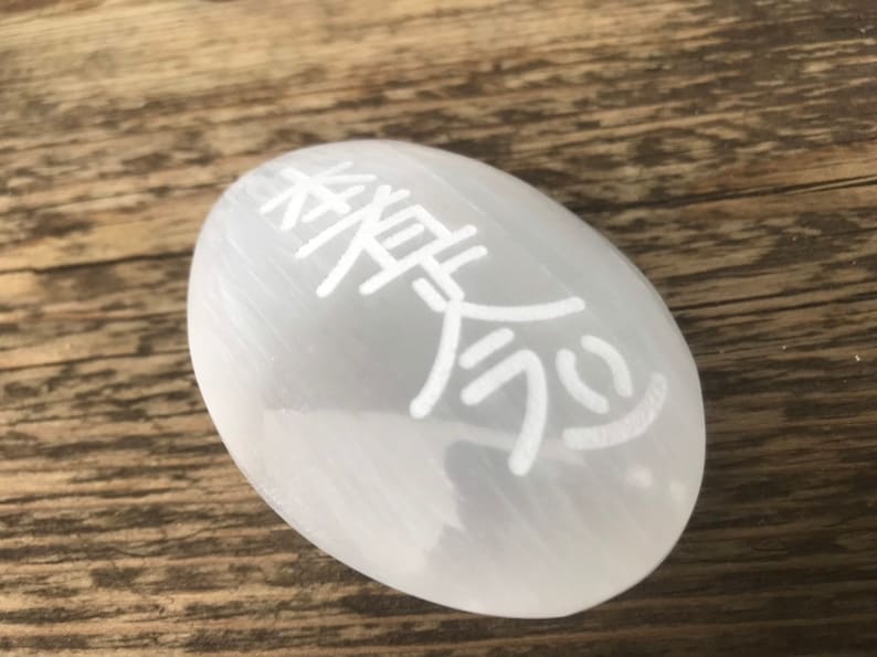 Pode incluir: Ovo de cristal de selenite branco com o s&iacute;mbolo chin&ecirc;s do "amor" gravado nele.