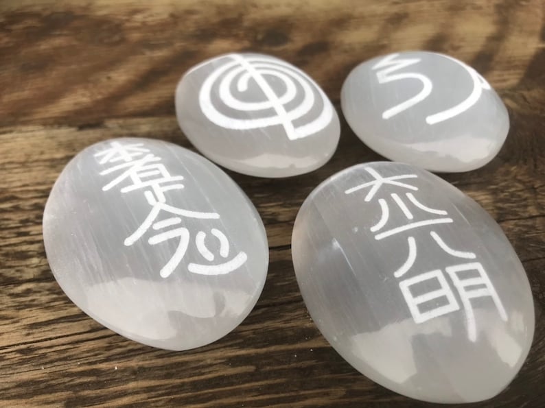 Pode incluir: Quatro pedras de selenita brancas com diferentes s&iacute;mbolos gravados. Os s&iacute;mbolos s&atilde;o uma espiral, um caractere chin&ecirc;s e dois caracteres japoneses diferentes.