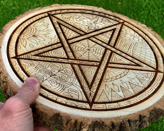 Puede incluir: Una rodaja de madera con un diseño de estrella de cinco puntas quemado en la superficie. La estrella está compuesta por diferentes patrones, incluyendo espirales, líneas y formas geométricas.