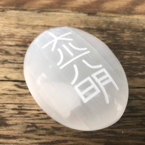 Pode incluir: Ovo de cristal de selenita branco com o s&iacute;mbolo chin&ecirc;s da "paz" gravado nele.