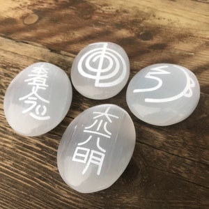 Pode incluir: Quatro pedras brancas de selenita com diferentes s&iacute;mbolos gravados nelas. Os s&iacute;mbolos s&atilde;o "Om", "Tai Chi", "Wu Xing" e "Hsing Shen".