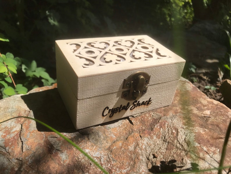 Pode incluir: Uma caixa de madeira branca com um design esculpido decorativo na tampa. A caixa tem uma trava de lat&atilde;o e as palavras "Crystal Shack" est&atilde;o gravadas na frente.