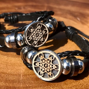 May include: Two black leather bracelets with silver metal beads and a wooden charm featuring a geometric design.