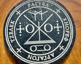May include: Black circular slate coaster with a silver inscription and a silver symbol in the center. The inscription reads "APLATON", "O.O", "X.HOPE.X", "TZBA.K", "RAGUEL", and "X".