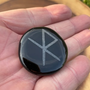 Runa de vínculo de viaje seguro grabada en una palma de obsidiana negra.