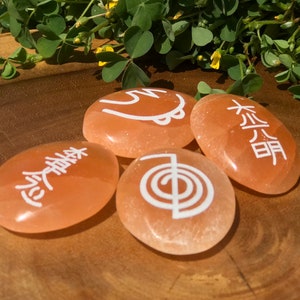 Pode incluir: Quatro pedras lisas de cor laranja com s&iacute;mbolos brancos. Os s&iacute;mbolos s&atilde;o uma espiral, uma &aacute;rvore, um c&iacute;rculo com uma linha que o atravessa e um s&iacute;mbolo que parece uma &aacute;rvore com uma linha que o atravessa.
