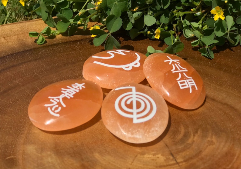 Pode incluir: Quatro pedras lisas de cor laranja com s&iacute;mbolos brancos. Os s&iacute;mbolos s&atilde;o uma espiral, uma &aacute;rvore, um c&iacute;rculo com uma linha que o atravessa e um s&iacute;mbolo que parece uma &aacute;rvore com uma linha que o atravessa.