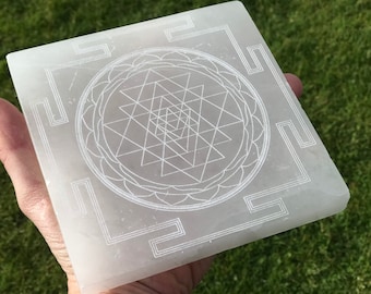 Puede incluir: Losa de cristal de selenita blanca con un diseño geométrico Sri Yantra grabado. El diseño es un mandala complejo con un triángulo central y múltiples capas de triángulos.