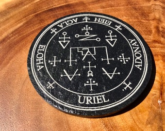 May include: Black circular stone with a white inscription that reads "URIEL" in the center. The inscription is surrounded by a circle of white text that reads "AGLA", "ELOHIA", "ADONAY", and "BEH", with symbols and markings in between.