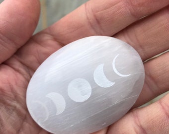 May include: White selenite palm stone with a moon phases design etched into the surface.