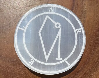 May include: White selenite stone with a white etched sigil of a geometric shape with a circle inside. The sigil is surrounded by a circle with the letters "A", "L", "E", "I", and "R" around the outside.