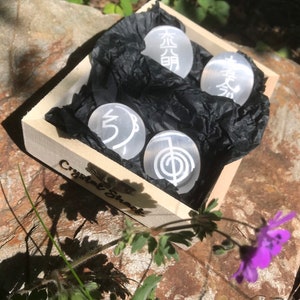 Pode incluir: Uma caixa de madeira com um forro de papel de seda preto, contendo quatro pedras de cristal brancas com s&iacute;mbolos gravados. A caixa est&aacute; etiquetada como "Crystal Shack".