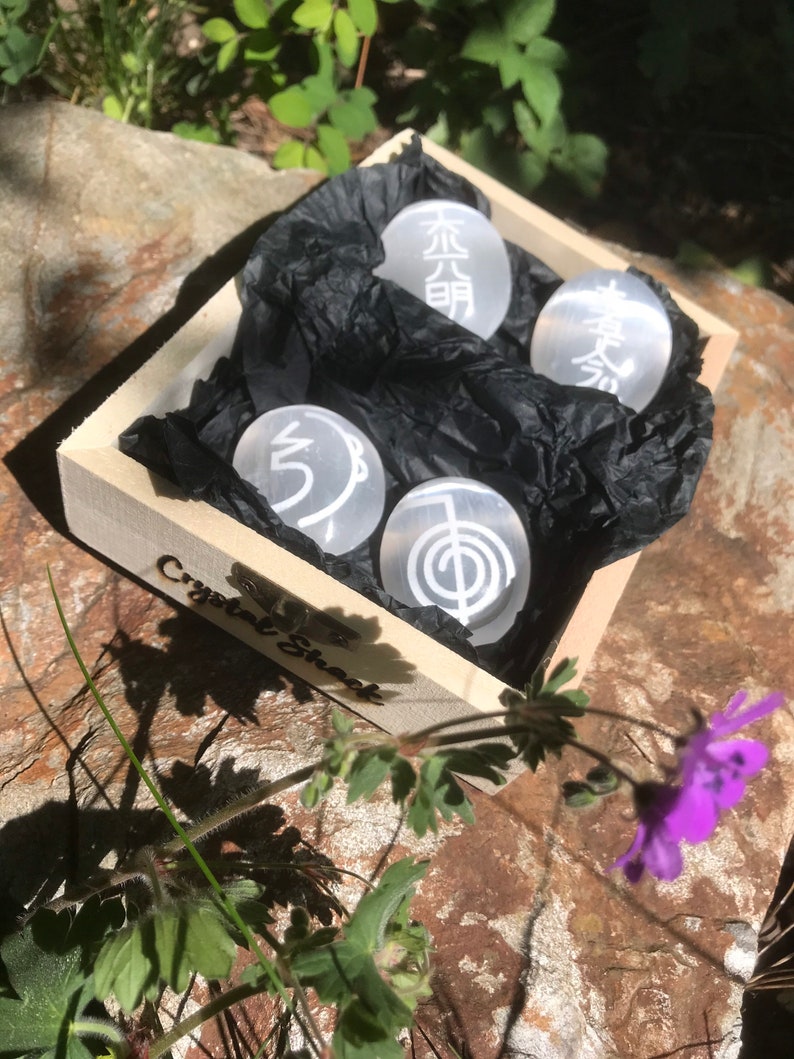 Pode incluir: Uma caixa de madeira com um forro de papel de seda preto, contendo quatro pedras de cristal brancas com s&iacute;mbolos gravados. A caixa est&aacute; etiquetada como "Crystal Shack".