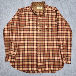 May include: A long-sleeve button-down shirt featuring a plaid pattern in shades of red, black, and tan. The shirt has a brown quilted inner collar lining with a visible tag that reads Lobo. It includes a single chest pocket and buttoned cuffs.