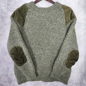 May include: A long-sleeve crew neck sweater in a heathered sage green knit fabric. The garment features contrasting dark olive green suede-like patches on the shoulders and rounded elbow patches on both sleeves, with a ribbed collar and cuffs.