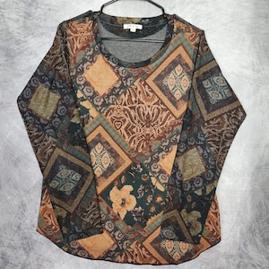 Op de afbeelding: Een shirt met lange mouwen van Orvis met een veelkleurig patchworkpatroon met geometrische vormen, bloemmotieven en Griekse sleutelranden in tinten bruin, beige, groenblauw en crème, voorzien van een ronde halslijn en een gebogen zoom.