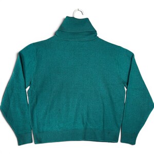 May include: A solid teal green long-sleeve sweater featuring a high turtleneck collar. The garment is constructed with a knit texture, long sleeves with ribbed cuffs, and a matching ribbed hemline at the bottom, presented on a simple hanger.