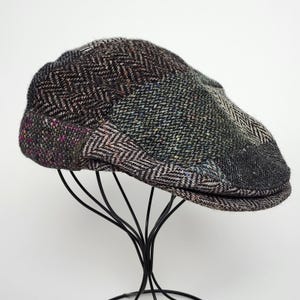 Puede incluir: Una gorra plana confeccionada con múltiples paneles de tejido de mezcla de lana que presenta una combinación de patrones de espiga y tweed en tonos carbón, gris, marrón y negro con sutiles motas púrpuras, azules y verdes en el material.