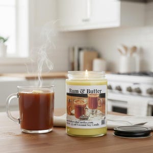 Puede incluir: Una vela en frasco de vidrio transparente con cera amarilla y una etiqueta que dice Rum & Butter, junto a una taza de vidrio humeante con líquido marrón oscuro. La vela tiene una mecha encendida y una tapa de metal negro sobre una servilleta.
