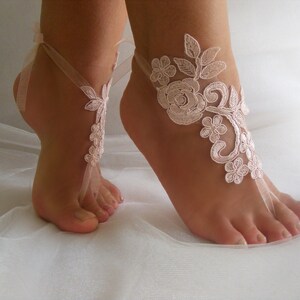May include: A pair of delicate, white lace barefoot sandals with a floral design. The sandals are tied with a ribbon around the ankle and have a delicate, feminine look.