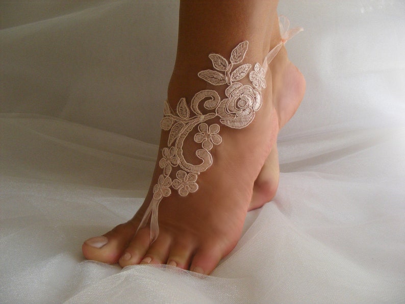 May include: A delicate ivory lace foot jewelry with floral designs. The lace is tied around the ankle and has a ribbon that ties around the toes.