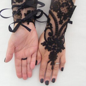 May include: A pair of black lace wrist cuffs with ribbon ties. The cuffs are made of delicate black lace with a floral pattern. The cuffs are tied with black satin ribbon.