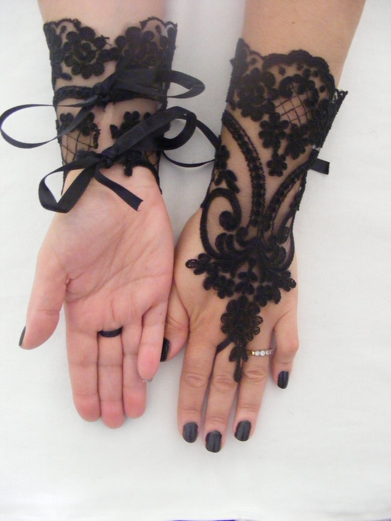 May include: A pair of black lace wrist cuffs with ribbon ties. The cuffs are made of delicate black lace with a floral pattern. The cuffs are tied with black satin ribbon.