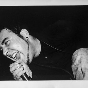 May include: Black and white photo of a person singing into a microphone. The person is wearing a black shirt and has a microphone in their hand. The person's mouth is open and they are singing.
