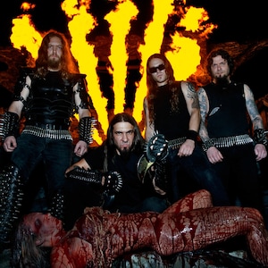 May include: Four men in black clothing stand in front of a fiery background. A woman lies on the ground covered in blood. The men are wearing leather jackets, belts, and studded gloves. The woman is wearing a white shirt and a brown belt. The background is a fiery orange and yellow.