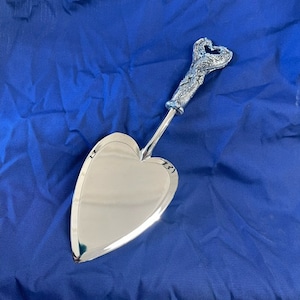 May include: A silver heart-shaped cake server with a detailed, ornate handle. The handle is shaped like a heart and has a floral design.