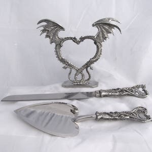 May include: Silver wedding cake knife and server set with dragon handles. The stand features two dragons intertwined in a heart shape.