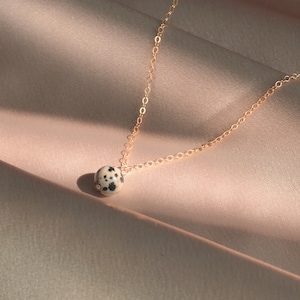 May include: A gold chain necklace with a round, black and white dalmatian jasper pendant.