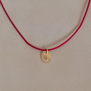 May include: A red string necklace with a gold charm featuring a crescent moon design.