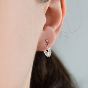 May include: A pair of small hoop earrings made of tiny white beads. The earrings are worn in a person's ear.