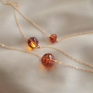 Peut inclure: Trois cha&icirc;nes en or avec des perles d'ambre. Les cha&icirc;nes sont superpos&eacute;es et les perles sont de tailles diff&eacute;rentes. Les perles sont d'une couleur orange fonc&eacute;.