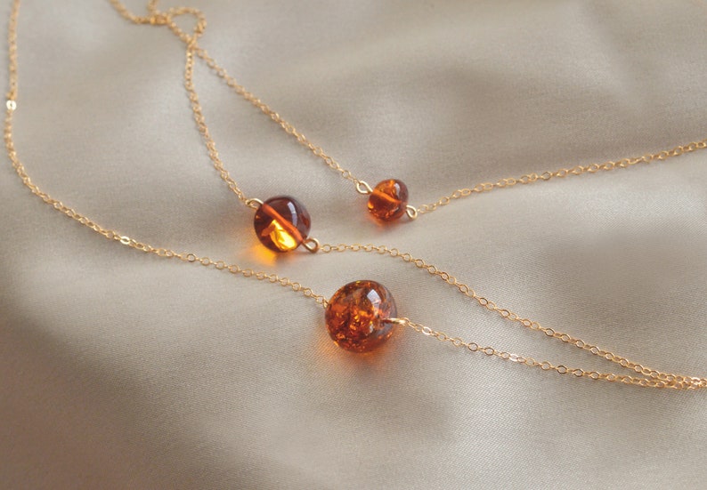Peut inclure: Trois cha&icirc;nes en or avec des perles d'ambre. Les cha&icirc;nes sont superpos&eacute;es et les perles sont de tailles diff&eacute;rentes. Les perles sont d'une couleur orange fonc&eacute;.