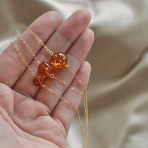 Peut inclure: Un collier en cha&icirc;ne dor&eacute;e avec trois perles d'ambre. Les perles sont rondes et ont un aspect naturel et organique.